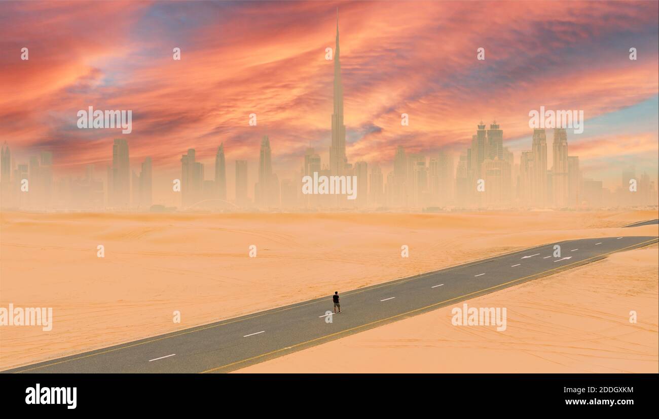Blick von oben, atemberaubende Luftaufnahme einer Person, die auf einer verlassenen Straße mit Sanddünen und der Skyline von Dubai bei Sonnenuntergang in der Ferne läuft. Stockfoto