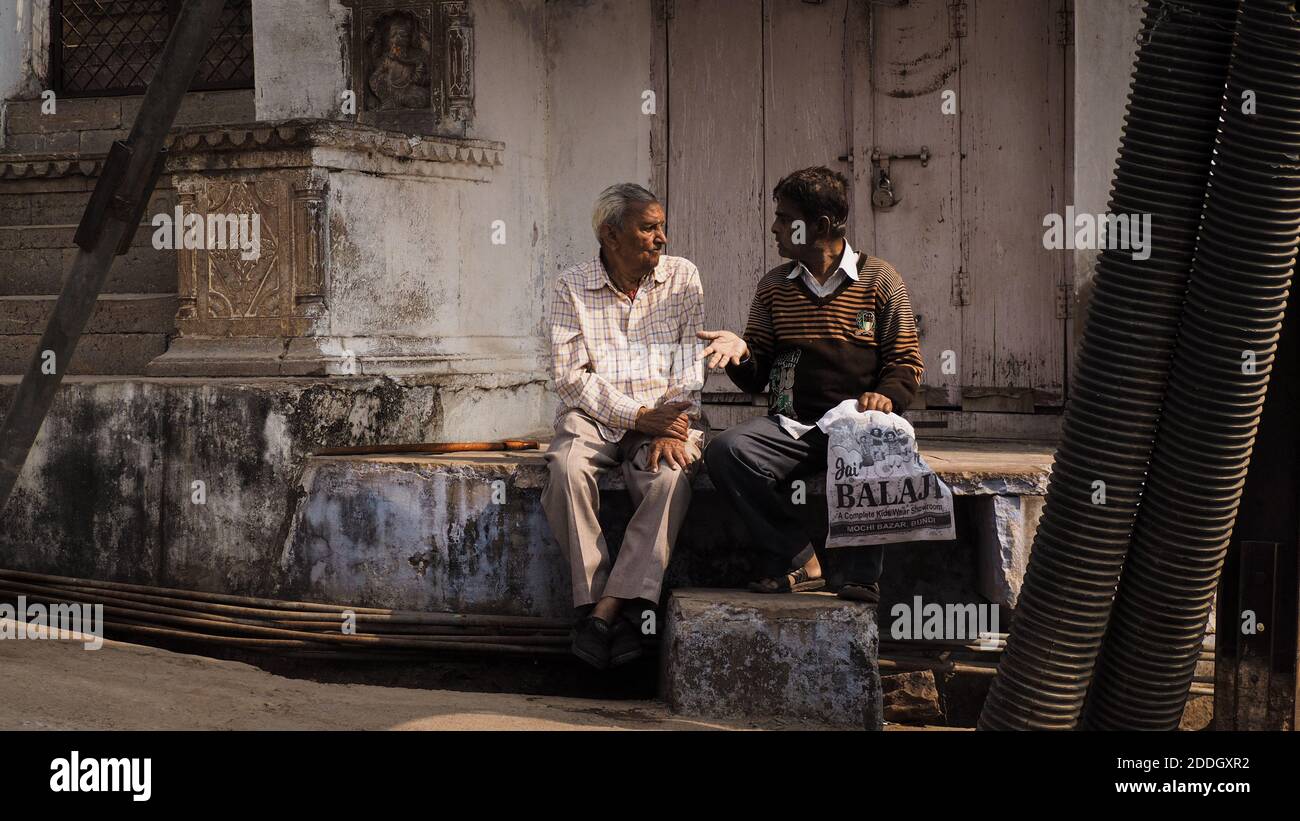 Zwei Männer sitzen und unterhalten sich an einer Straßenecke in Bundi, Indien. Stockfoto