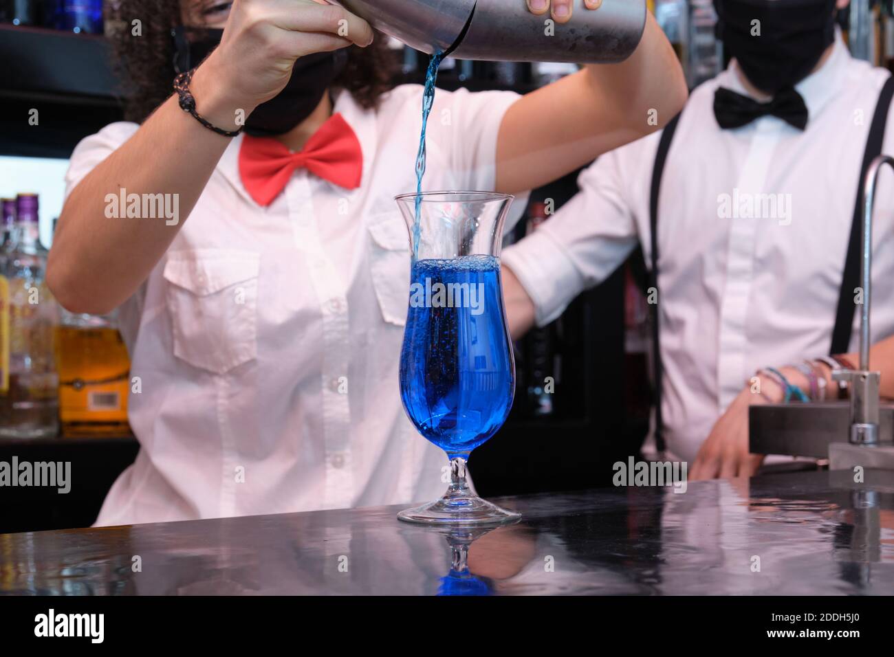 Nicht erkennbare Kellnerin trägt eine schützende Gesichtsmaske und bereitet Cocktails in einem Pub zu. Neue Normalität in Pubs. Stockfoto