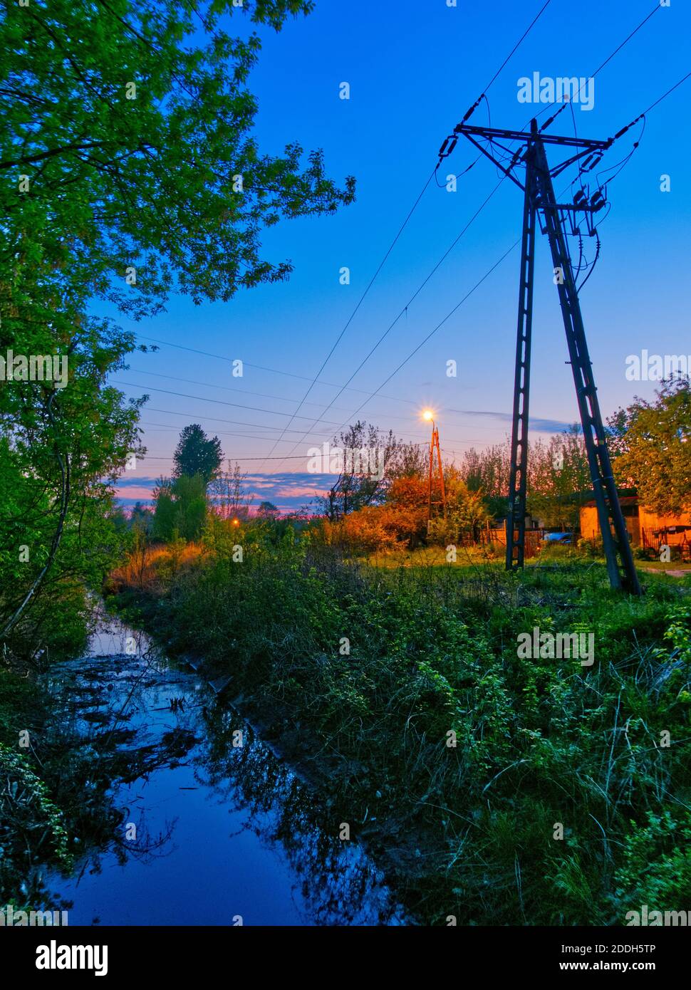 Vertikale Foto in einem Abend mit blau gesättigten Himmel mit Wasserstrom und Strom Pylon in der Nähe stehen gemacht. Stockfoto