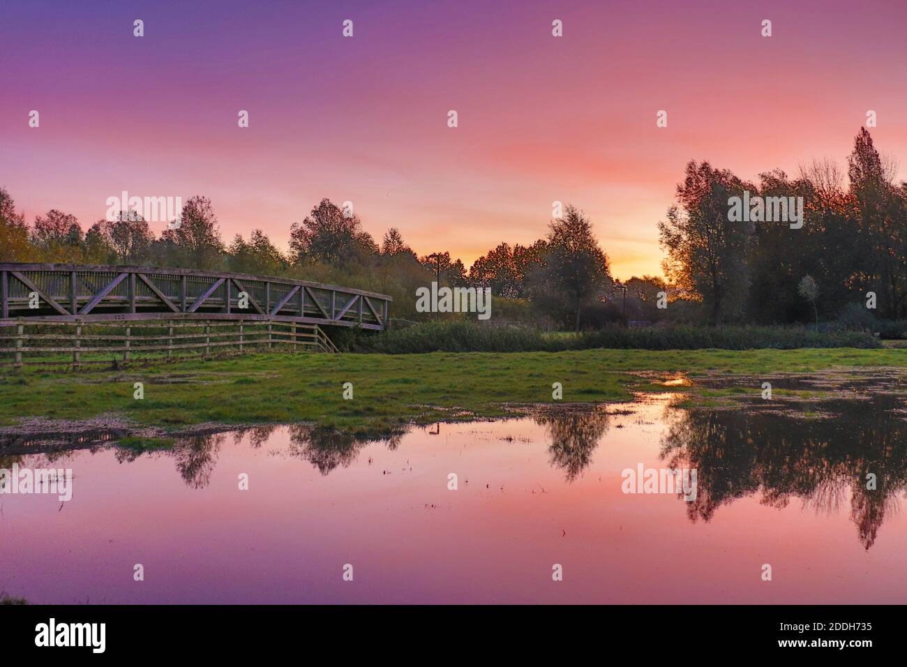 Ein farbenprächtiger Sonnenaufgang, der sich vom Flutwasser reflektiert, grenzt an eine Fußgängerbrücke in Milton Keynes. Stockfoto