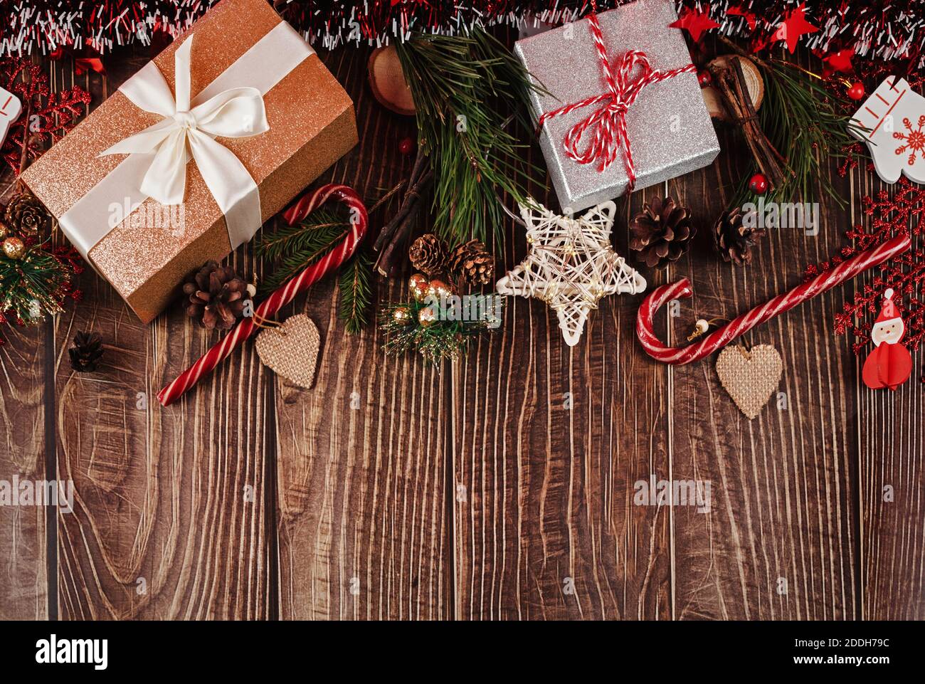 Geschenkschachteln in Glitzerverpackung, Lametta, Tannenbaum, Zapfen, Zuckerstöcke und weihnachtsdekorationen auf dunklen Holzbrettern. Feiertagshintergrund mit niedriger Stockfoto