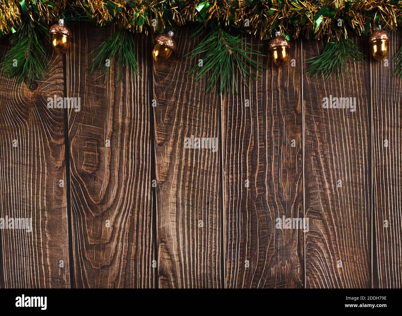 Dunkle Holzbretter Hintergrund mit schimmernden grünen und gelben Lametta, Tannenzweigen und Glas weihnachtsdekorationen in Form von goldenen Eicheln. Ne Stockfoto