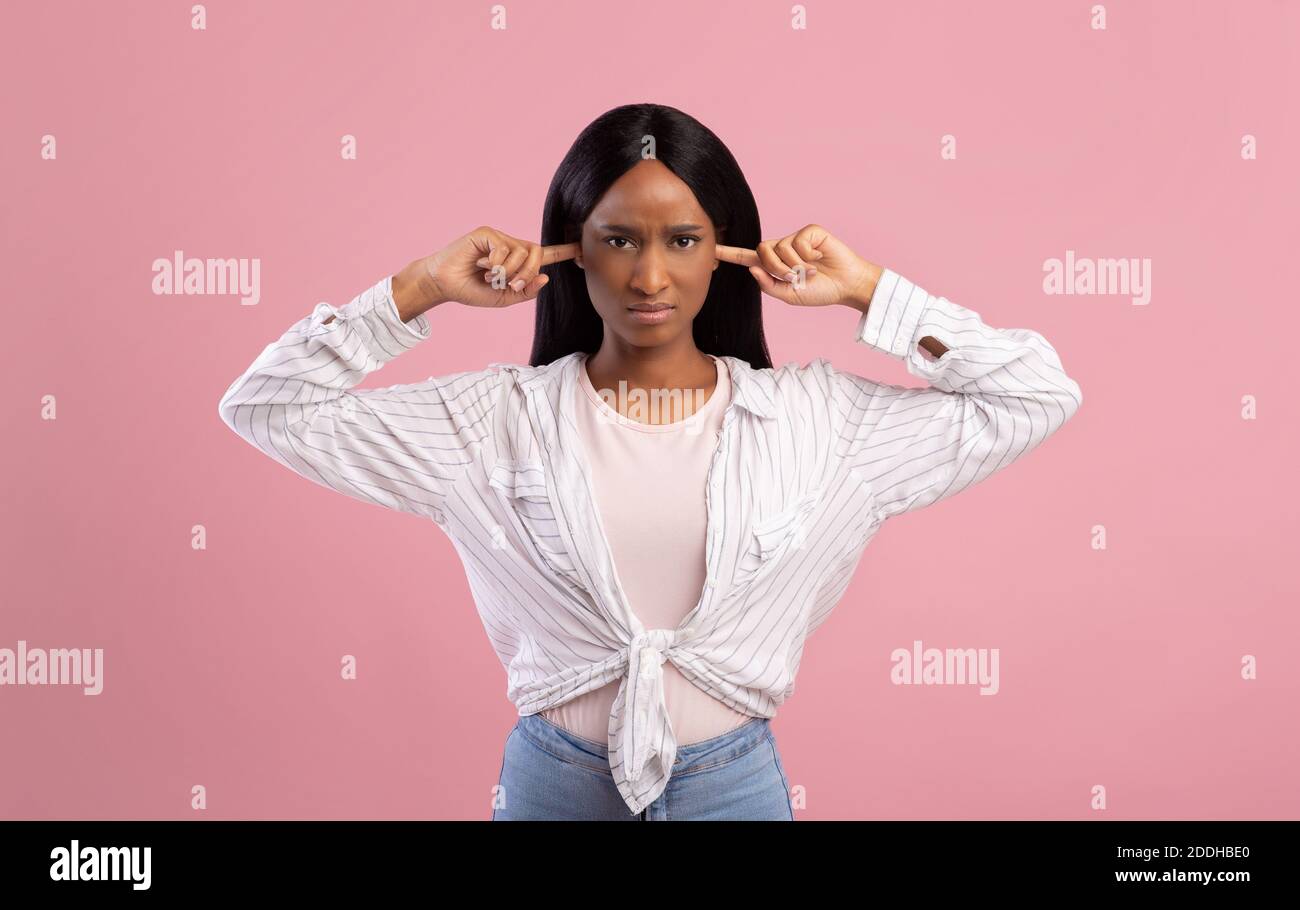 Verärgert schwarze Dame schließt ihre Ohren mit den Fingern, Schutz vor lauten Lärm auf rosa Studio Hintergrund Stockfoto