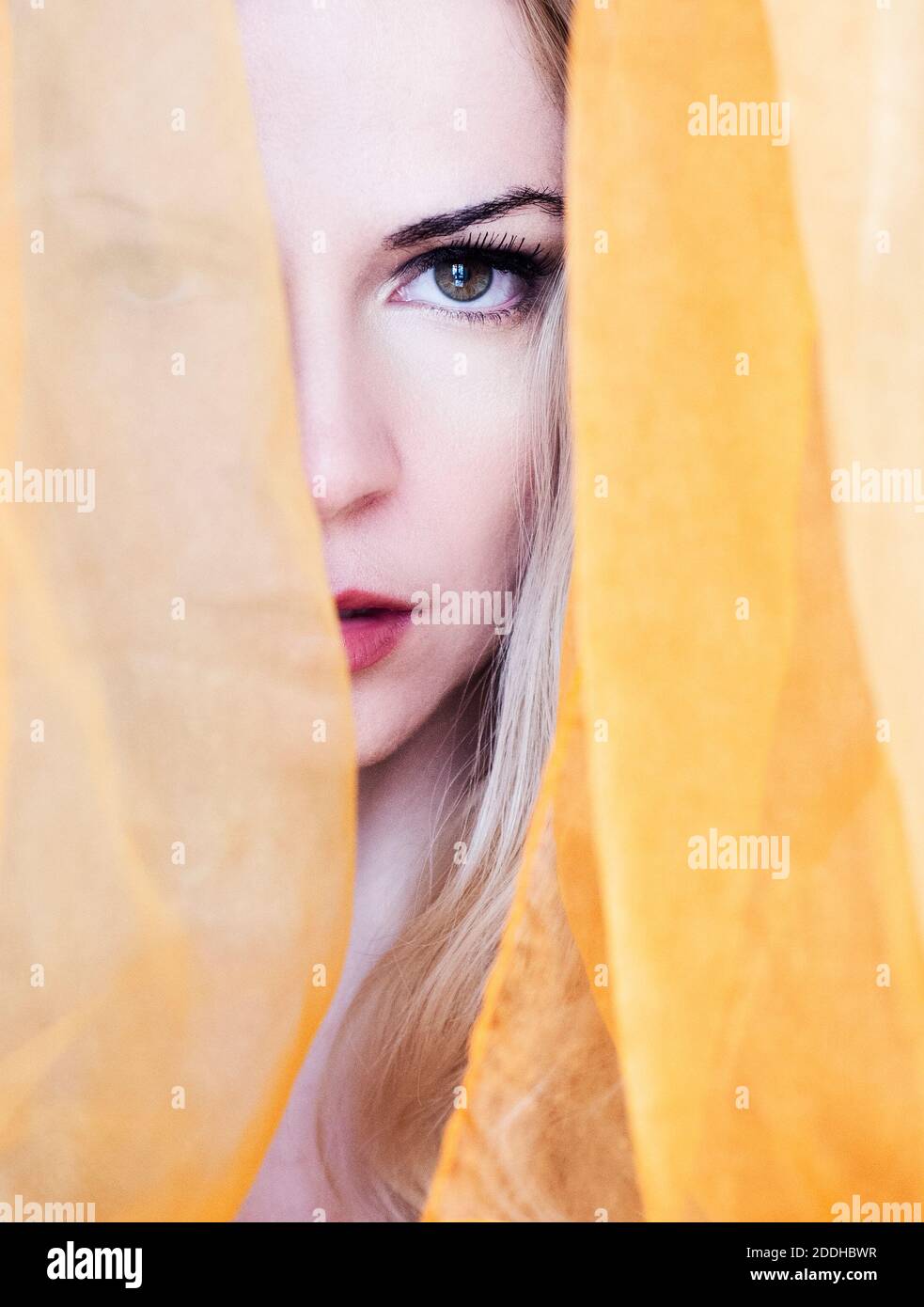 Schöne Frau mit langen blonden Haaren guckt von zwischen gelb Vorhang Stockfoto