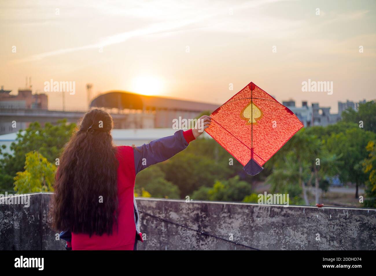 Junge Frau hält hoch bunte Papier und Holz Drachen gegen Ein verschwommener Hintergrund, der die Sonne auf dem indischen Drachenfest untergeht Von makar sankranti oder Stockfoto