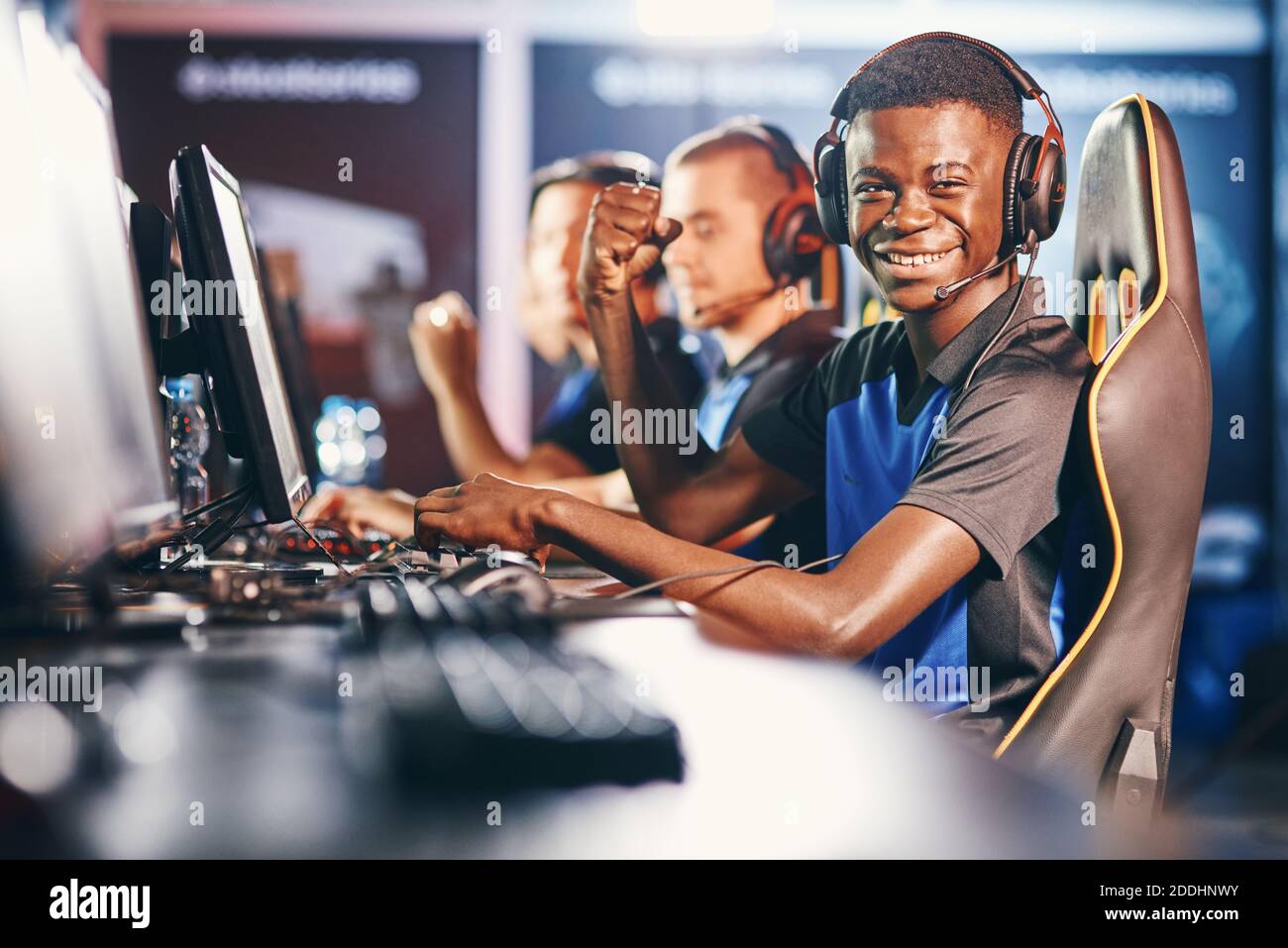 Seitenansicht eines fröhlichen afrikaners, professioneller Cybersport-Gamer, der Kopfhörer trägt und die Kamera anschaut und lächelt, während er mit dem Team am eSport-Turnier teilnimmt. Videospiele Online-Wettbewerb Stockfoto