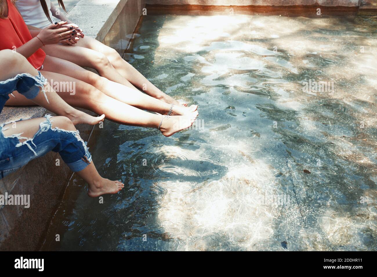 Beine von drei Frauen sitzen am Brunnen Stockfoto