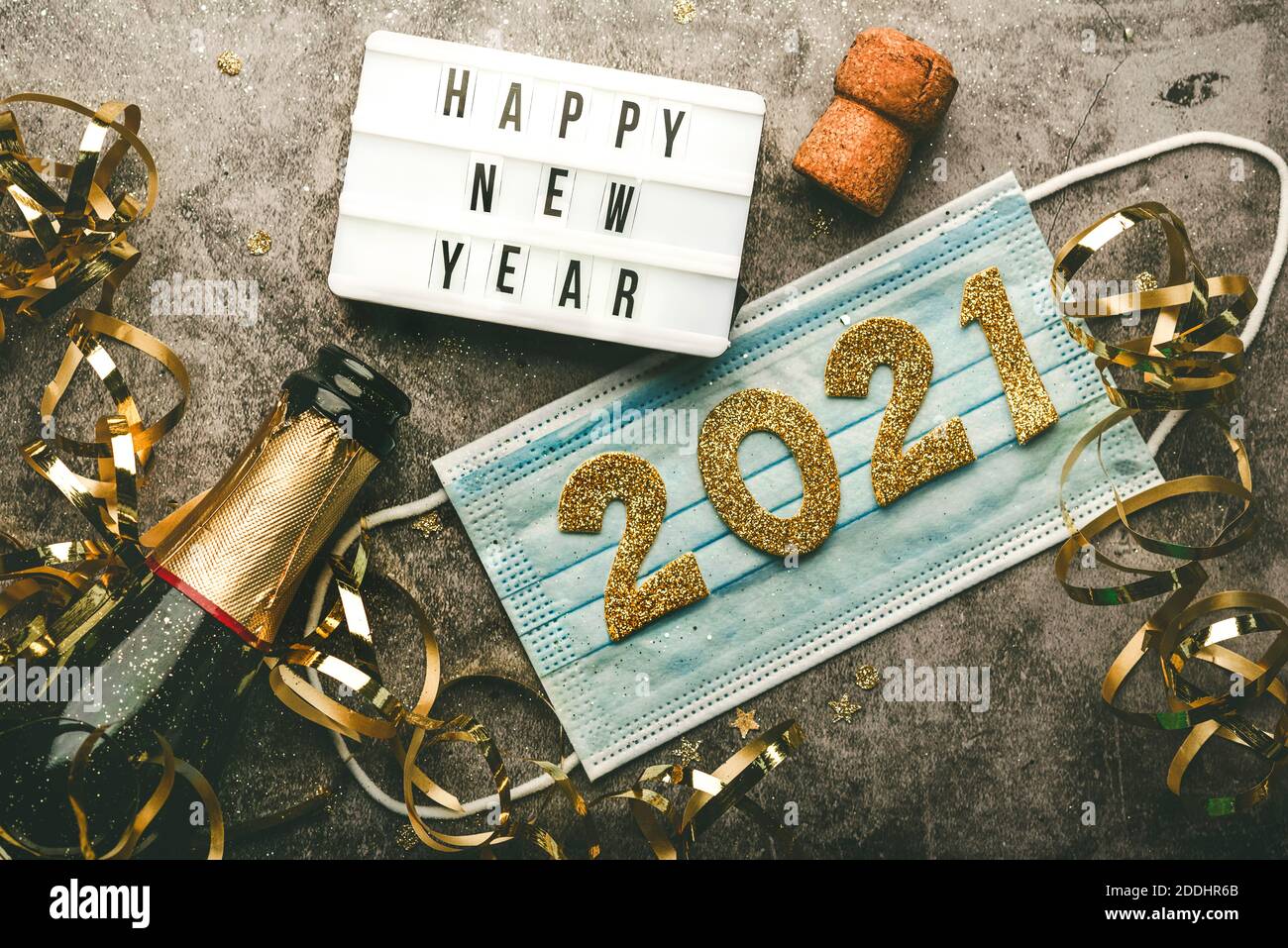 Silvester Feier Konzept Hintergrund.Medizinische Maske und Leuchtkasten mit Text frohes neues Jahr.Covid-19 Neujahrskonzept auf grauem Hintergrund Stockfoto