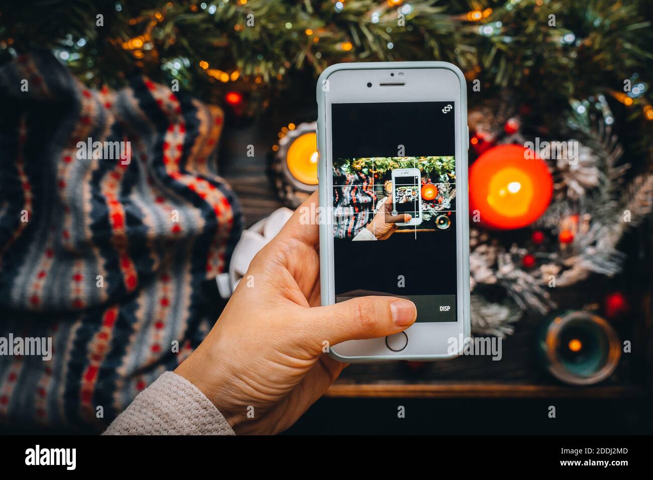 Frau Hand halten Telefon Foto von Weihnachten Tisch flach legen, rote Geschenk Geschenke Box, Ornamente, gemütliches Zuhause, Kerze auf Tapete, Postkarte greetin Stockfoto