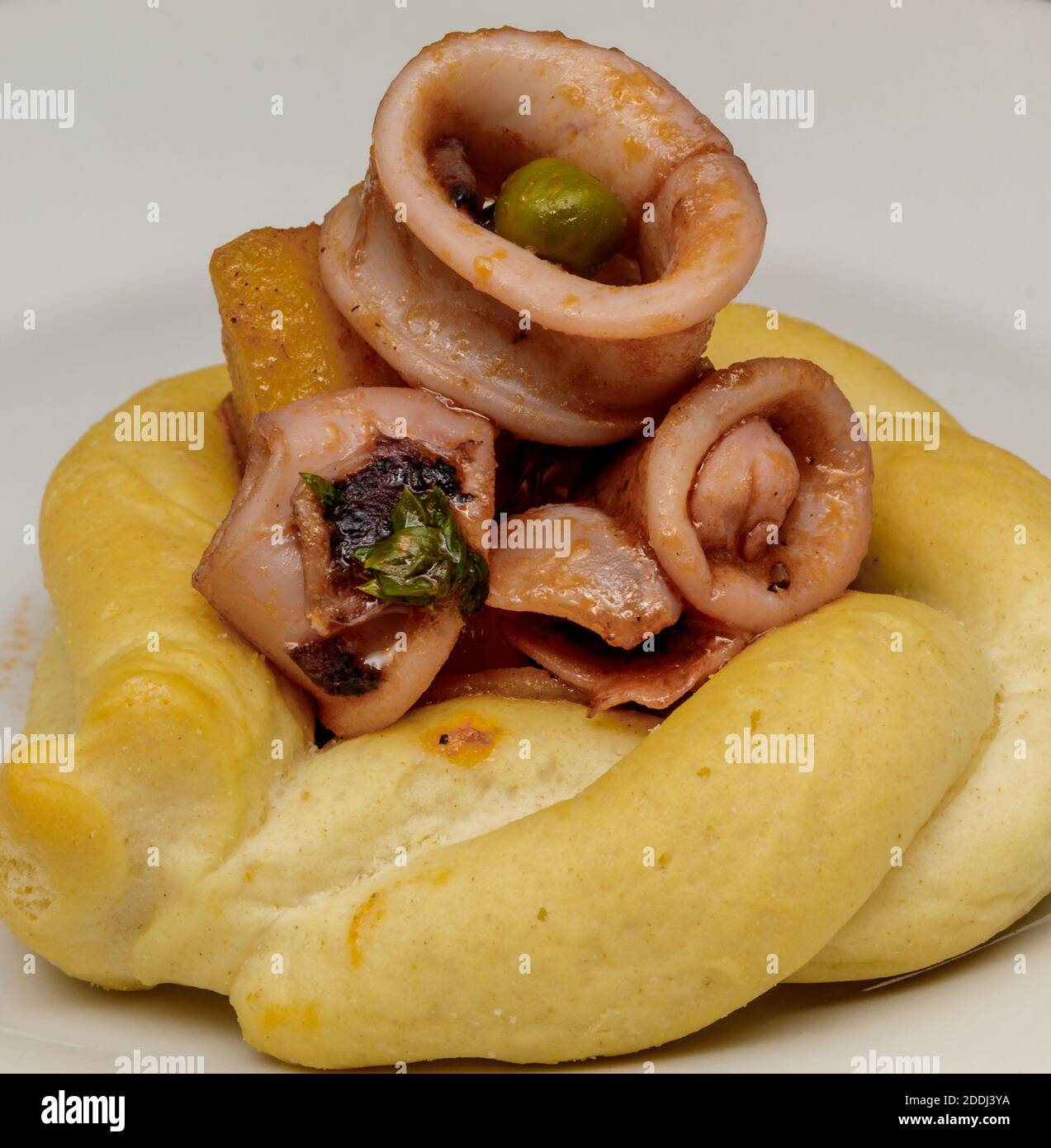 Geschmorte Calamari mit Erbsen, Kartoffeln, Zwiebeln, Petersilie, Tomaten, Pfeffer, Salz, Öl und Zitronenschale auf knusprigem Brot. Stockfoto