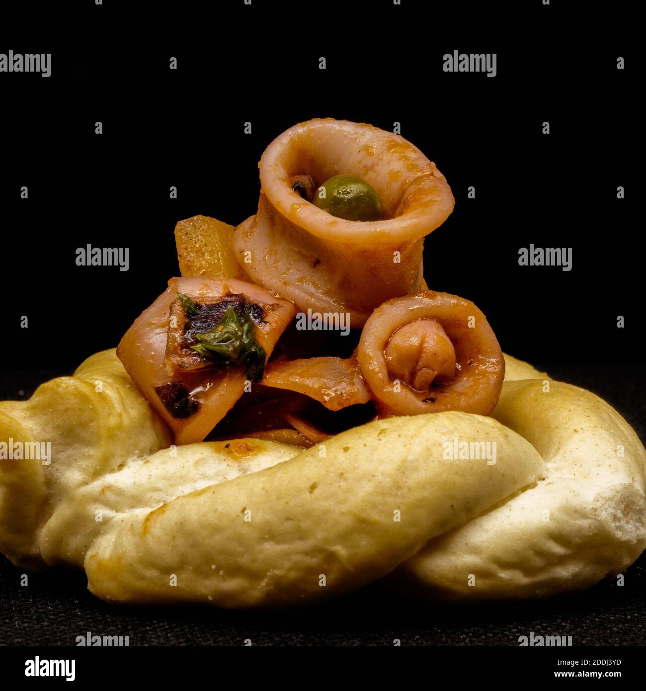 Geschmorte Calamari mit Erbsen, Kartoffeln, Zwiebeln, Petersilie, Tomaten, Pfeffer, Salz, Öl und Zitronenschale auf knusprigem Brot. Stockfoto