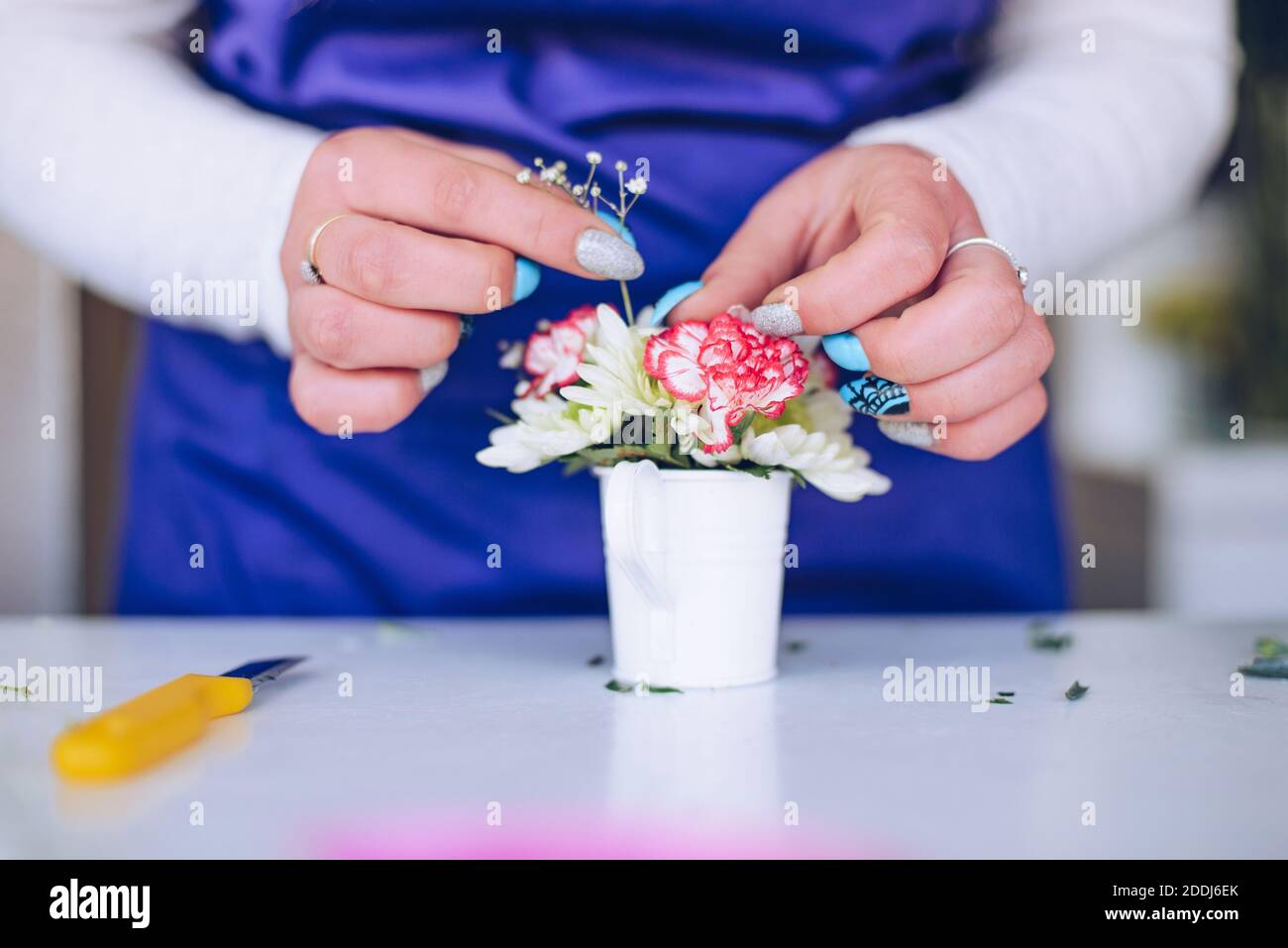 Die Floristen-Hände schaffen eine Komposition aus Blumen in einem kleinen weißen Topf. Stockfoto