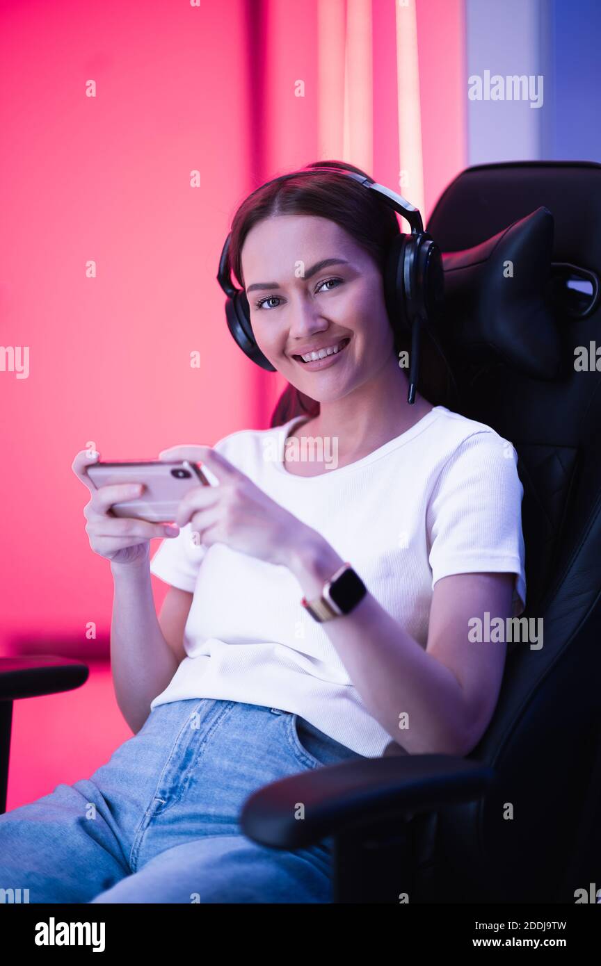 Cybersport Gamer spielen mobile Spiel auf dem Smartphone sitzen auf einem Gaming-Stuhl in Neon-Farbraum. Stockfoto