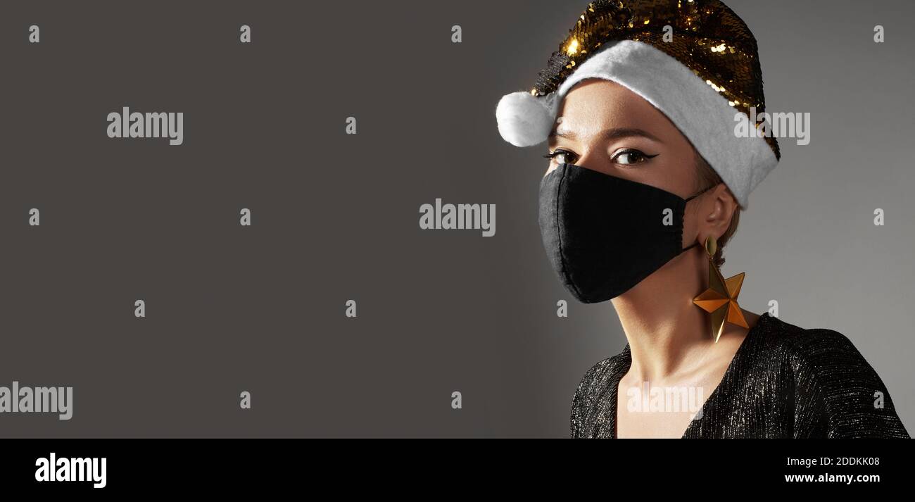 Frau mit goldenem weihnachtshut, schwarze medizinische Maske. Mode-Stil mit glänzenden Kleidung und Accessoires für Weihnachten Zeit. Schützen Sie sich vor Coronavirus C Stockfoto