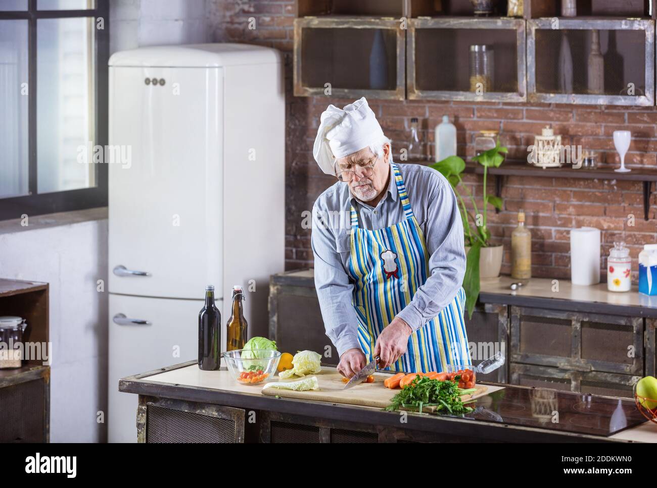 Senior Mann im Koch hat Hacken frisches Gemüse für Salat. Gesunde Essgewohnheiten. Stockfoto