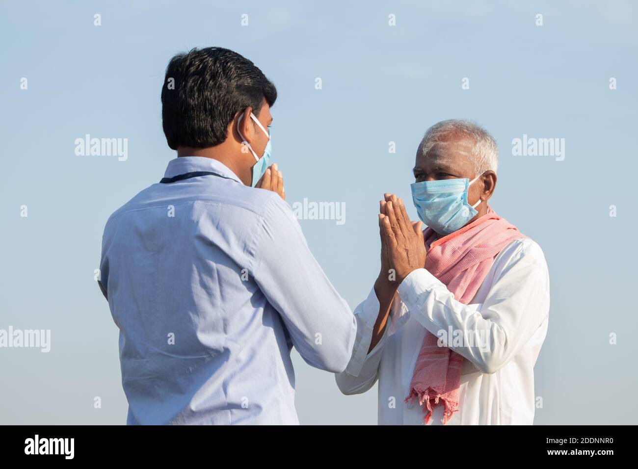 Low-Winkel-Ansicht, Farmer Gruß an Bankier oder Corporate Government Officer durch namaste tun, während beide Gesichtsmaske getragen wegen Coronavirus covid-19 Stockfoto