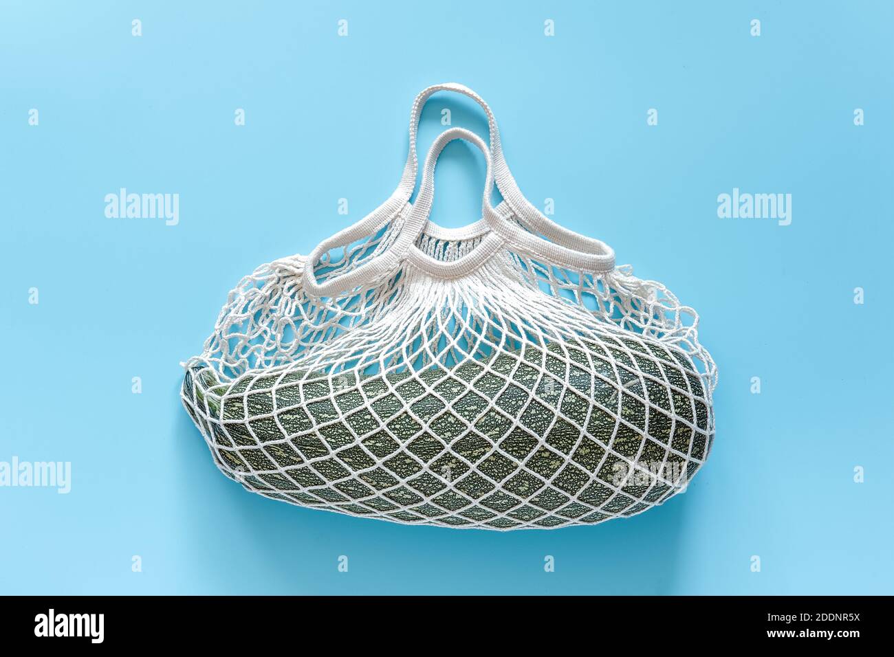 Frische Zucchini im wiederverwendbaren Einkauf umweltfreundliche Netztasche auf blauem Hintergrund. Konzept Bio Kürbis Gemüse und kein Kunststoff, keine Abfälle. Speicherplatz kopieren Stockfoto