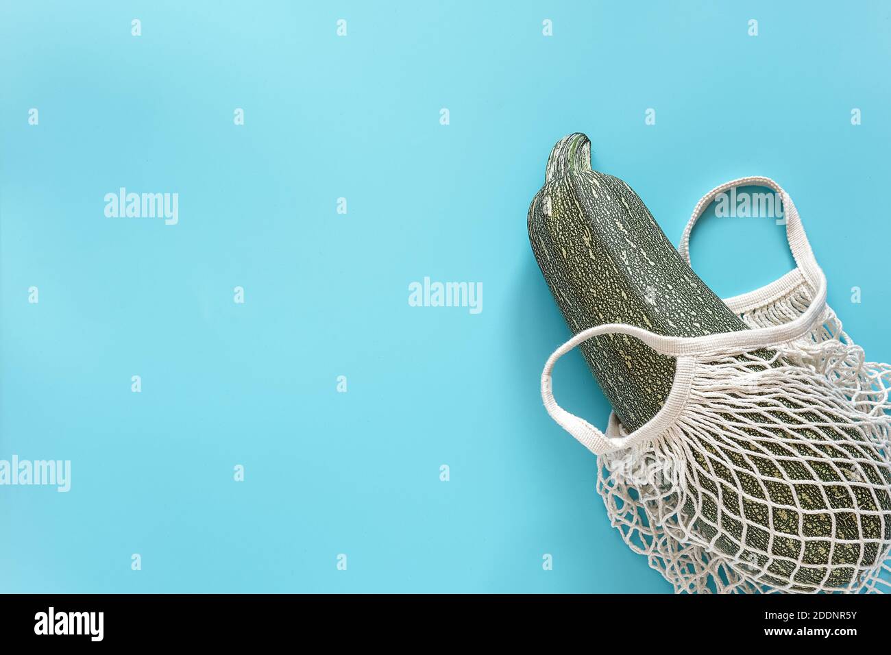 Frische Zucchini im wiederverwendbaren Einkauf umweltfreundliche Netztasche auf blauem Hintergrund. Konzept Bio Kürbis Gemüse und kein Kunststoff, keine Abfälle. Speicherplatz kopieren Stockfoto