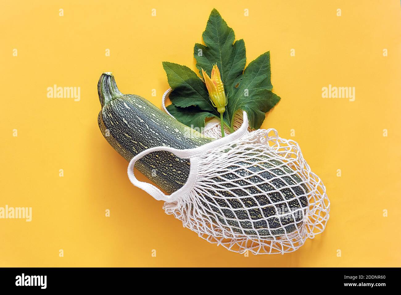 Frische Zucchini mit grünem Blatt und Blume im wiederverwendbaren Einkaufen umweltfreundliche Netztasche auf gelbem Hintergrund. Konzept Bio Squash Gemüse und kein pla Stockfoto