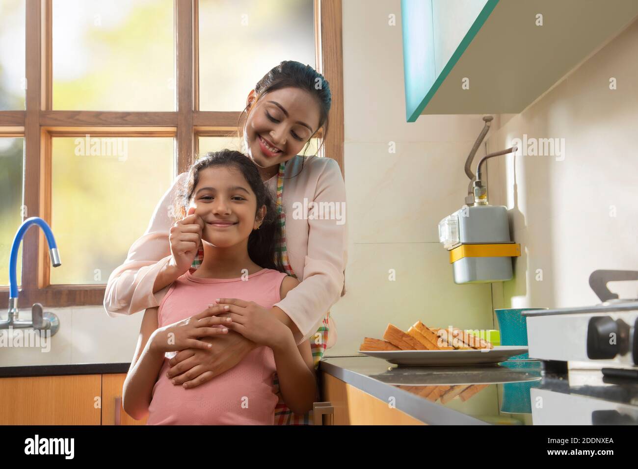 Mutter zieht liebevoll die Wangen der Töchter in die Küche Stockfoto