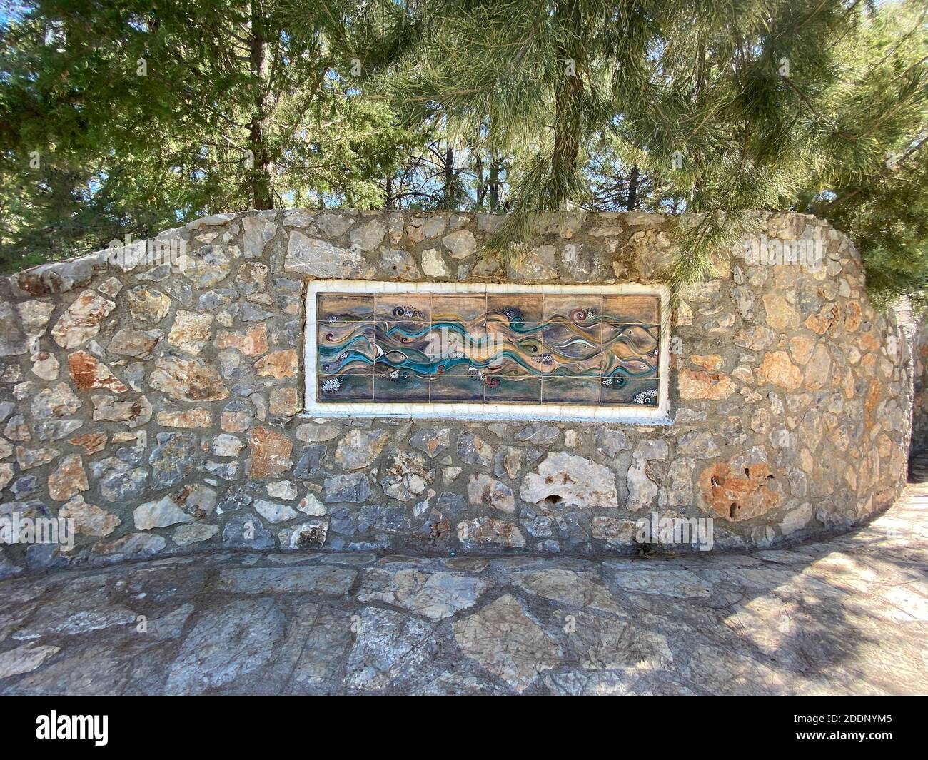 Glas und Malerei Wandkunst auf einer Außenwand aus Stein. Steinboden und Pinien im Hintergrund. Wasser- und Wellenmotiv. Stockfoto