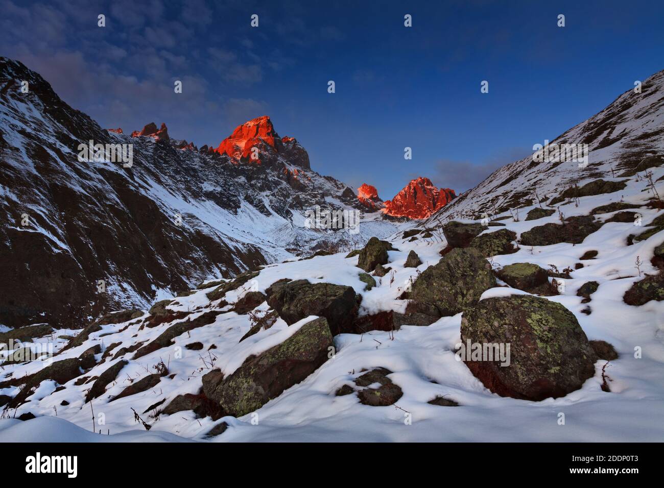 Atemberaubender Sonnenuntergang über Upper Svaneti, Greater Caucasus, Georgia, mit zwei Berggipfeln, die von rotem Licht beleuchtet werden. Schneebedeckte felsige Landschaft. Stockfoto