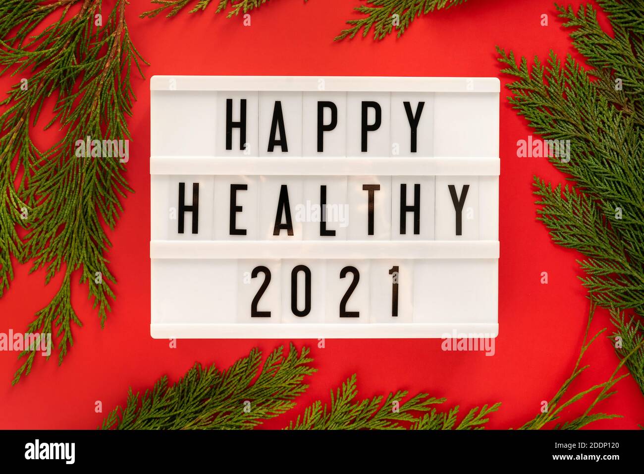 Happy Healthy 2021 Jahr auf einem weißen Vintage Leuchtkasten auf hellrotem Hintergrund mit Wacholderzweigen um, flach lag angezeigt. Stockfoto