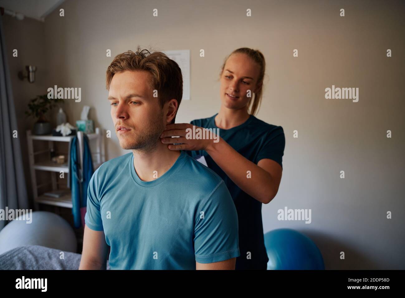 Junge weibliche Physiotherapeutin gibt Nackenmassage an männliche Patienten in Klinik Stockfoto