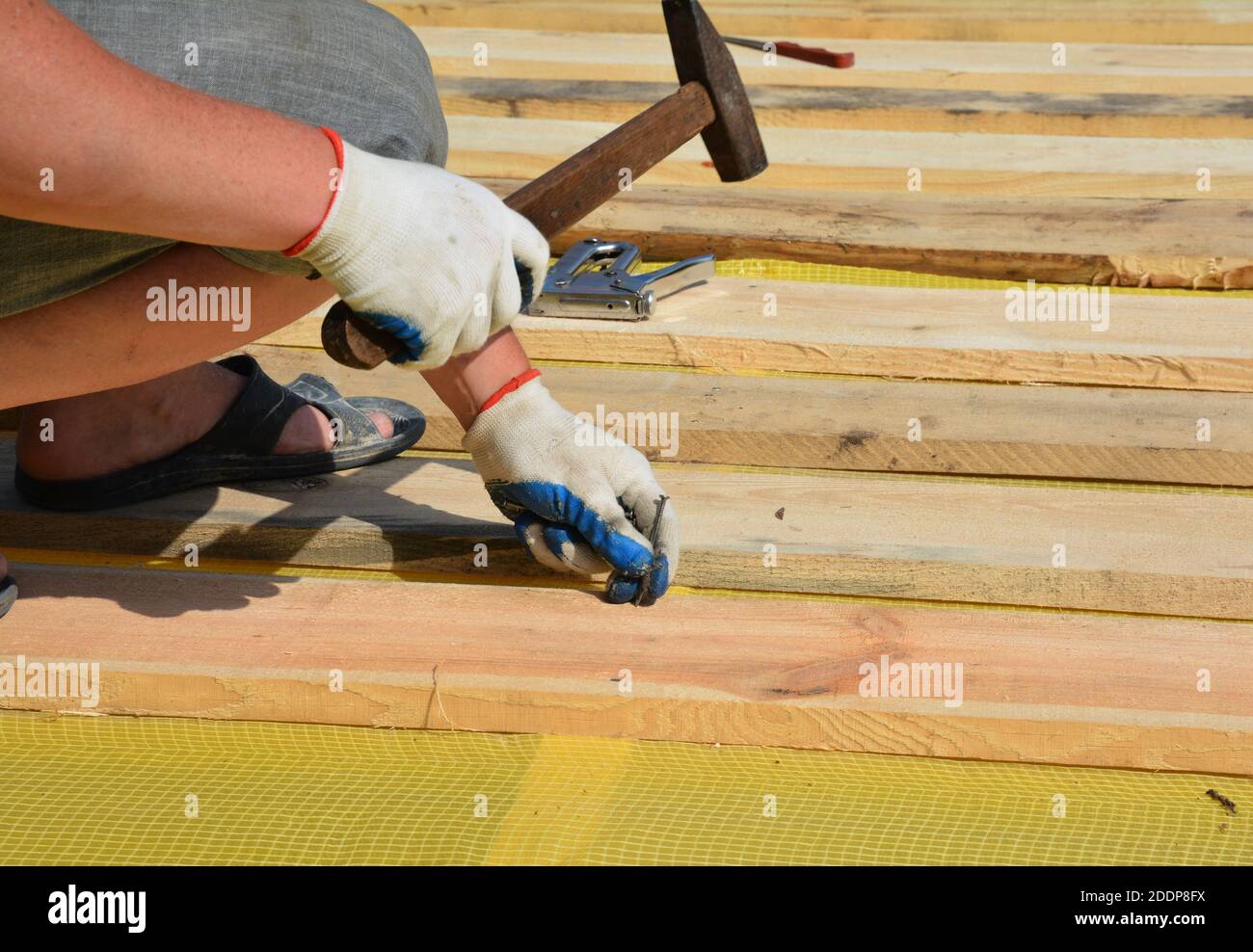 Ein Dachdecker installiert Holzverkleidung, Deck, Planken auf einer Dampfbarriere Membran mit einem Hammer und Nägeln, während Metall Dachkonstruktion. Stockfoto