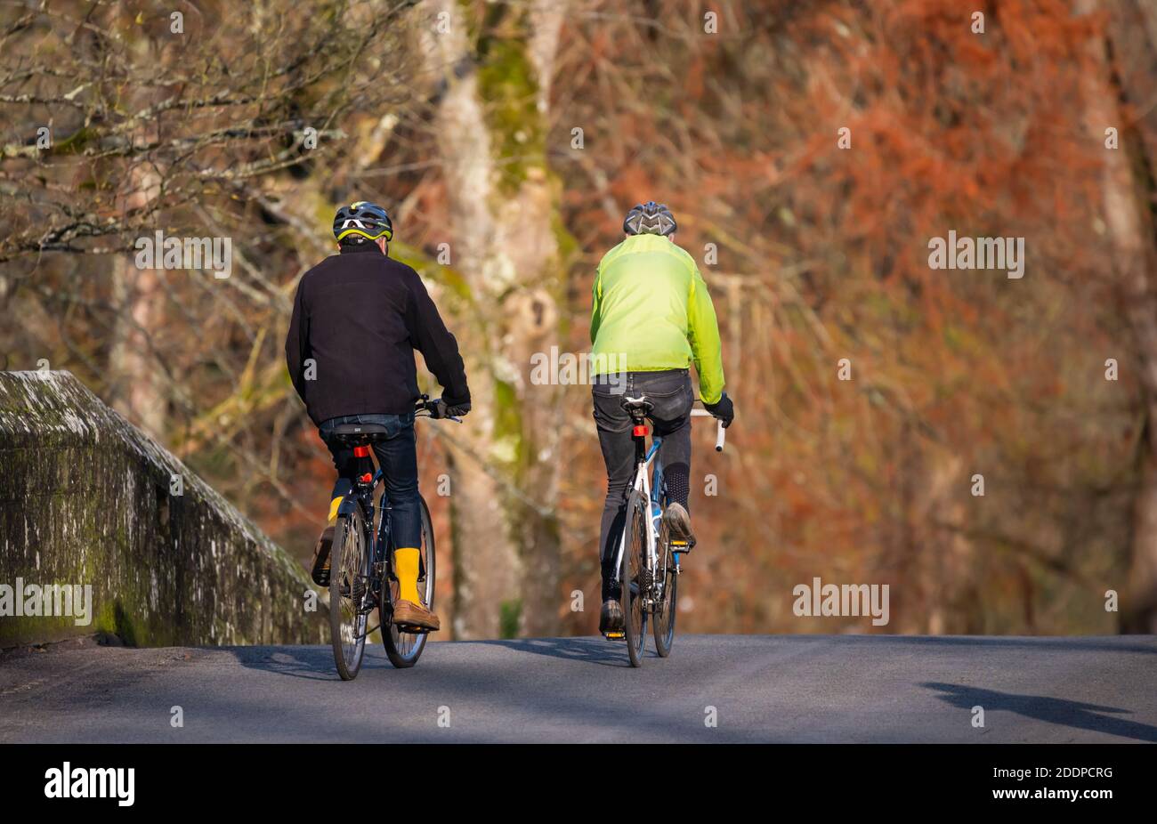 Zwei männliche Radfahrer, die über eine Brücke fahren und 2 verschiedene Helme tragen, in West Sussex, England, Großbritannien. Stockfoto