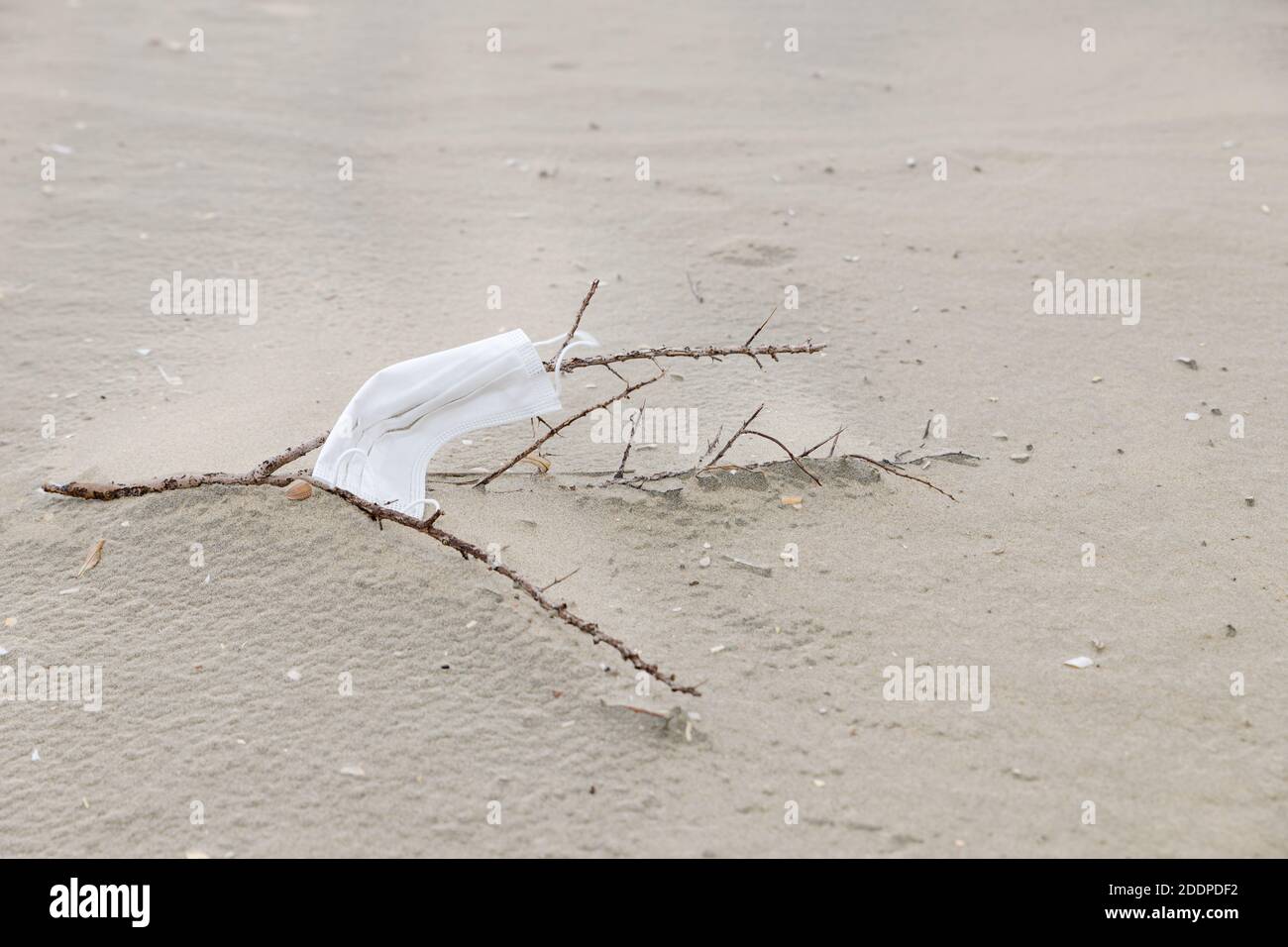 Eine Gesichtsmaske zum Schutz während der Covid-19 Pandemie wird am Strand zurückgelassen und verursacht Umweltverschmutzung. Stockfoto