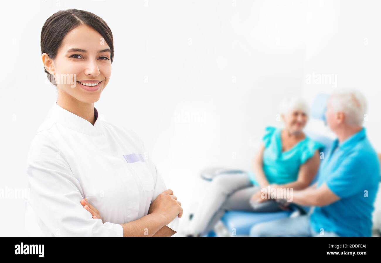 Lächelnde Ärztin, ältere Patienten sitzen hinter ihr zusammen. Porträt eines Arztes, auf dem Hintergrund alter Patienten Stockfoto Lächelnde Ärztin, ältere Patienten sitzen hinter ihr zusammen. Porträt eines Arztes, auf dem Hintergrund alter Patienten Stockfoto