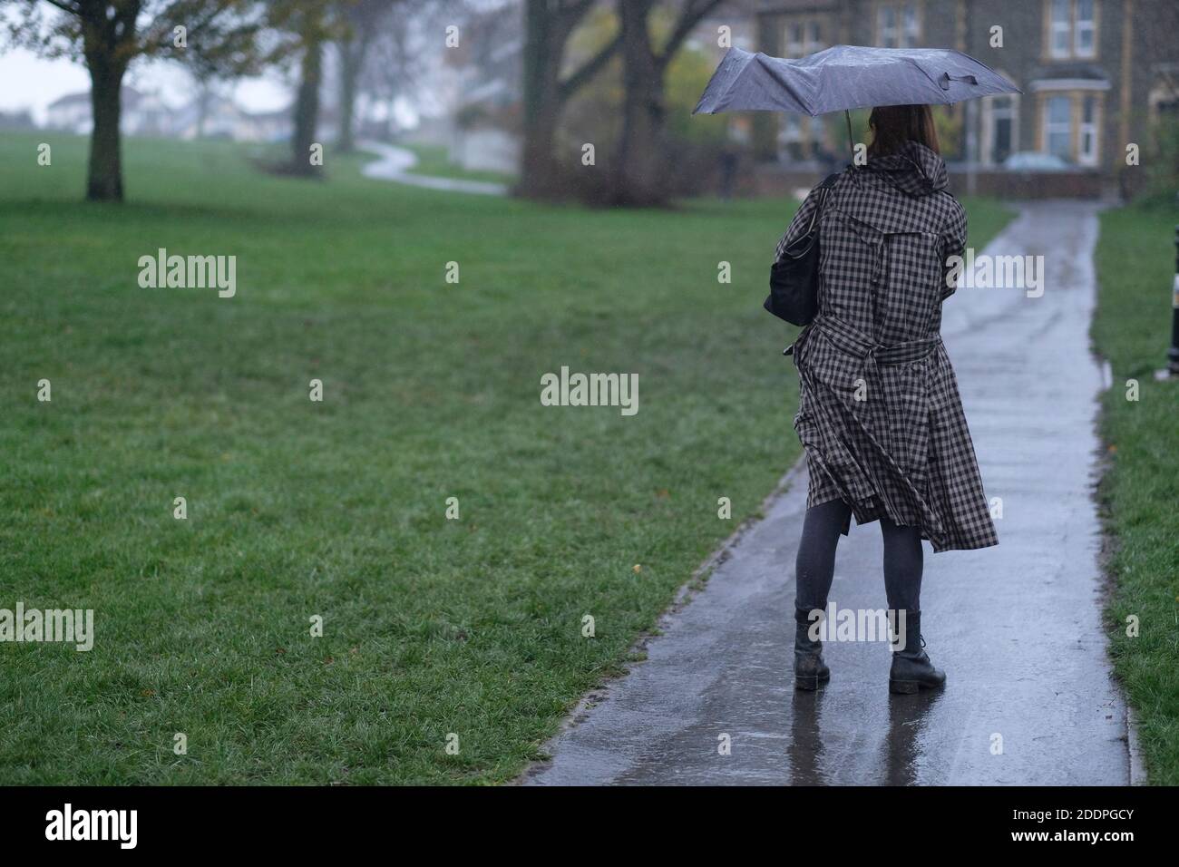 Eine Frau mit Regenschirm an einem regnerischen Tag mit einem kaputten Regenschirm. Stockfoto