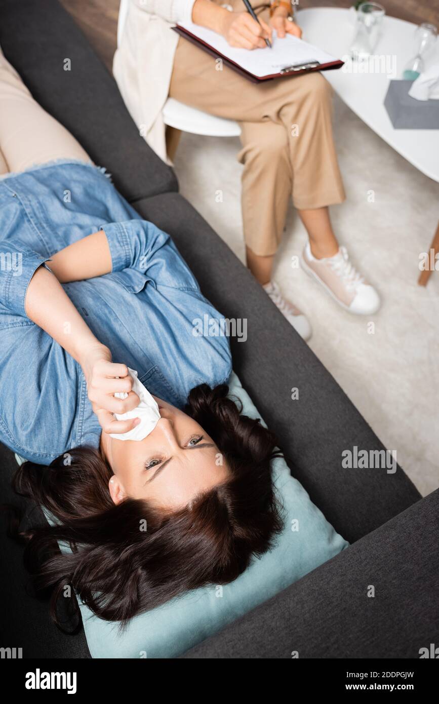 Brunette Frau wipping Nase mit Gewebe, während Therapeut Notizen machen Stockfoto