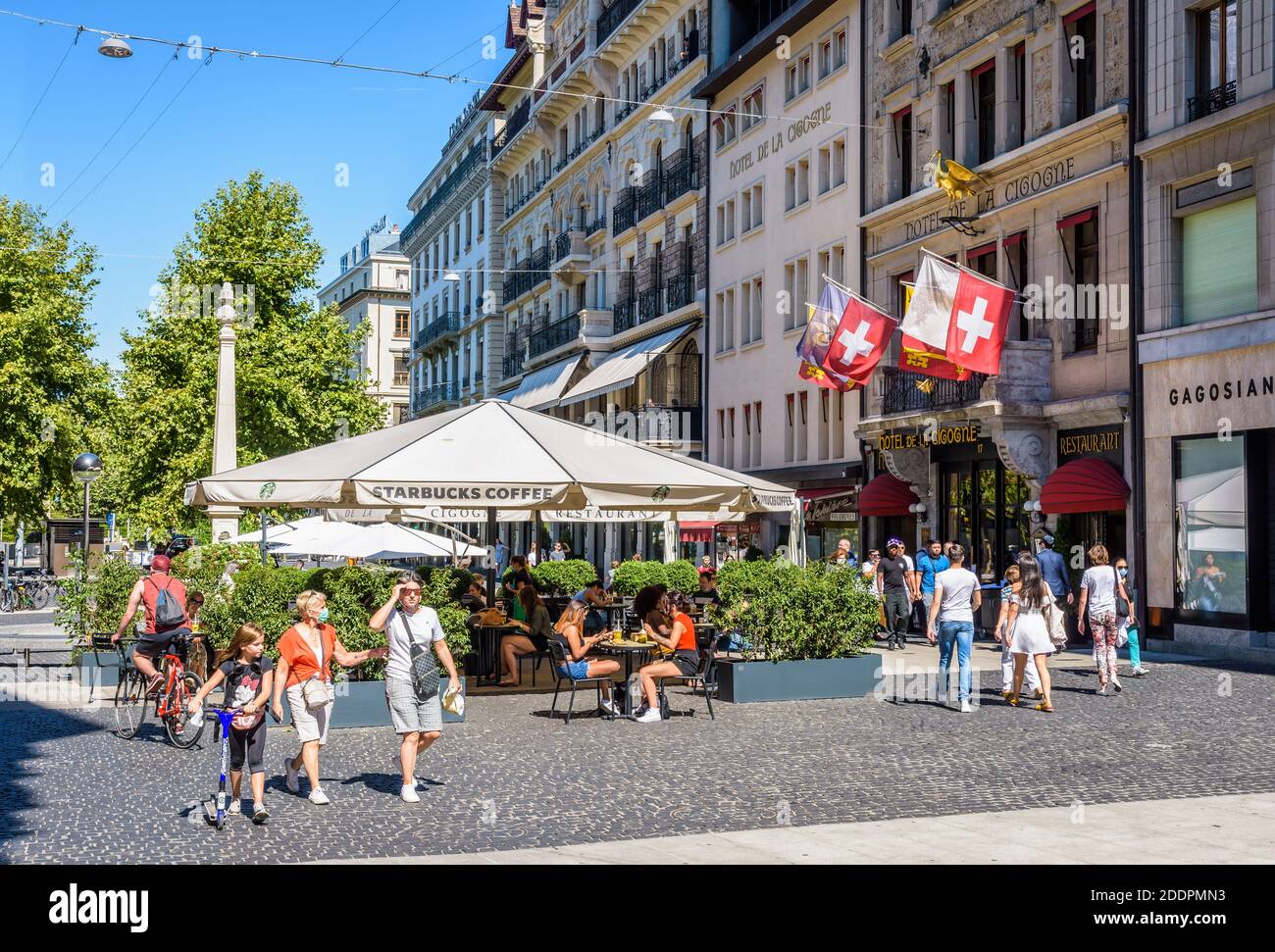 Leute, die auf der Terrasse eines Starbucks Coffee auf dem Place de Longemalle in Genf spazieren oder einen Drink genießen, vor dem Hotel de la Cigogne. Stockfoto