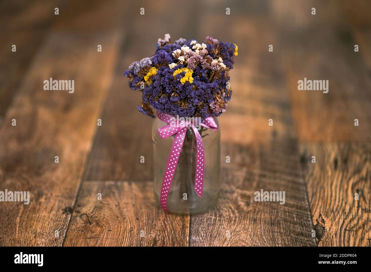 Ein Bouquet von getrockneten Blumen, Limonium sinuatum, Wellenblatt Meer Lavendel, Statice, Notch Blatt Sumpf Rosmarin, Meer rosa in einem Glas, rosa Band, Holzboden Stockfoto