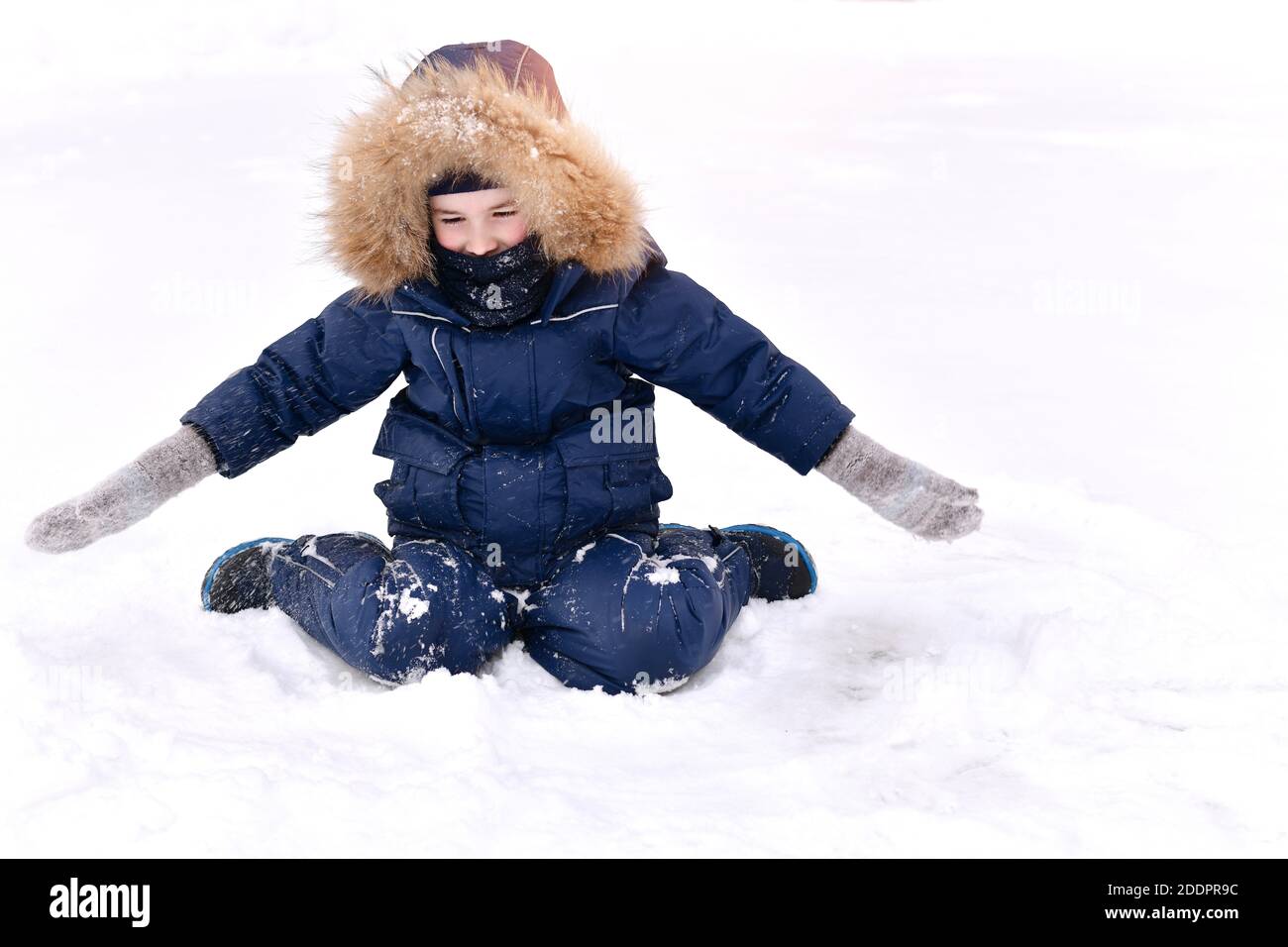Das Kind ist warm gekleidet, mit einer Pelzhaube und einer Balaclava-Gamasche, die vor dem Frost schützt. Sitzt mit offenen Armen in Fäustlingen und sieht mit Überraschung Stockfoto