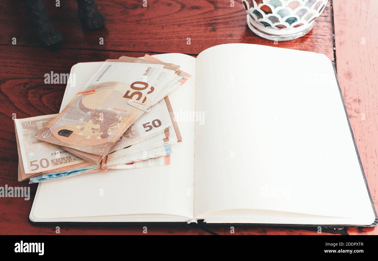 Geldbündel auf offenem Notizbuch gegen alten Holzschreibtisch Stockfoto