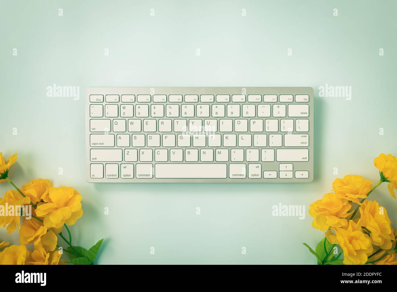Weiße, tragbare Computer-Tastaturtasten oder Tastaturtaste und gelbe Tasten Blume unten auf Blau Pastell minimalistischen Hintergrund in Vintage Ton Stockfoto