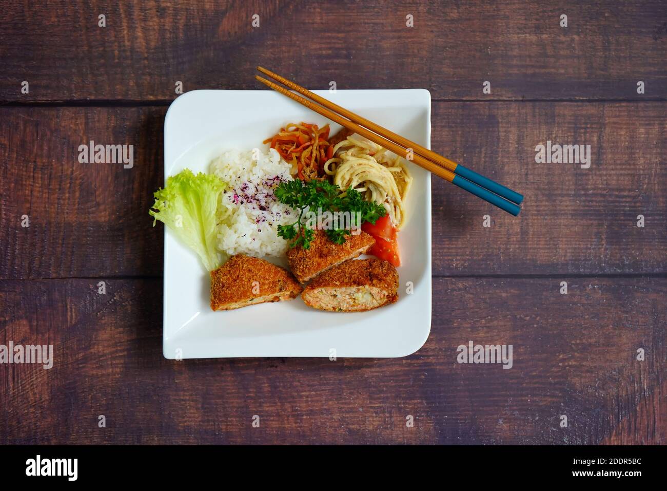 Japanischer Lachs Fischkuchen, Reis, Nudelsalat und Gemüse auf einem weißen Teller. Rustikale dunkle Holztisch Hintergrund. Stockfoto