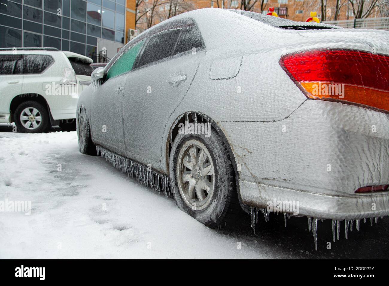 Der graue Pkw war nach dem nassen Regen in der Stadt im Winter mit einer dicken Eiskruste bedeckt. Stockfoto