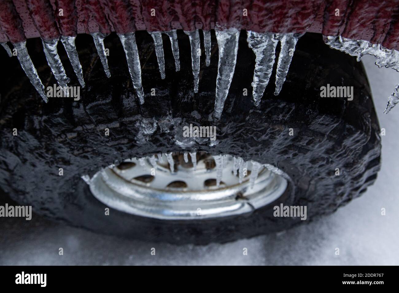 Der rote Kotflügel und das Rad des SUV sind durch den Regen im Winter sehr eisig. Eiszapfen hängen herunter. Stockfoto