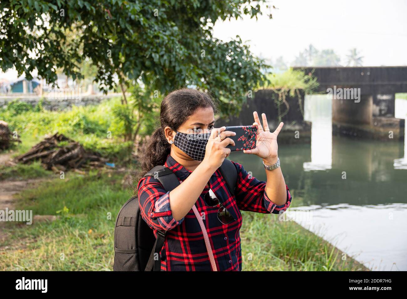 Kadamakudy Kerala Rucksack Explorer Frauen tragen Gesichtsmaske fotografieren Mit ihrem Telefon auf weiß verschwommen grünen Hintergrund verschwommen Stockfoto