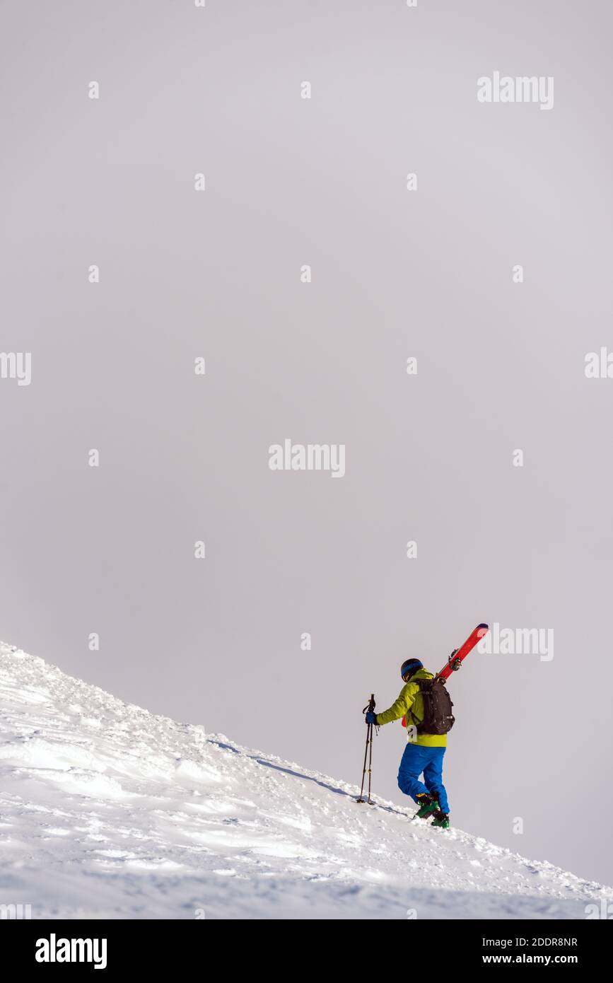 Skifahrer, die zu Fuß einen Berg erklimmen und dabei den Himmel abseits der Piste tragen. Der bewölkte Himmel sorgt für einen perfekten neutralen Hintergrund Stockfoto