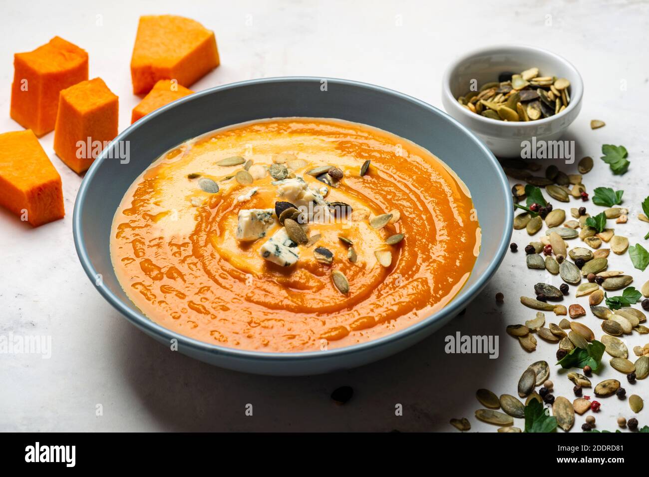 Kürbiscremesuppe mit Käsen und Samen in der Schüssel auf weißem Grund. Stockfoto