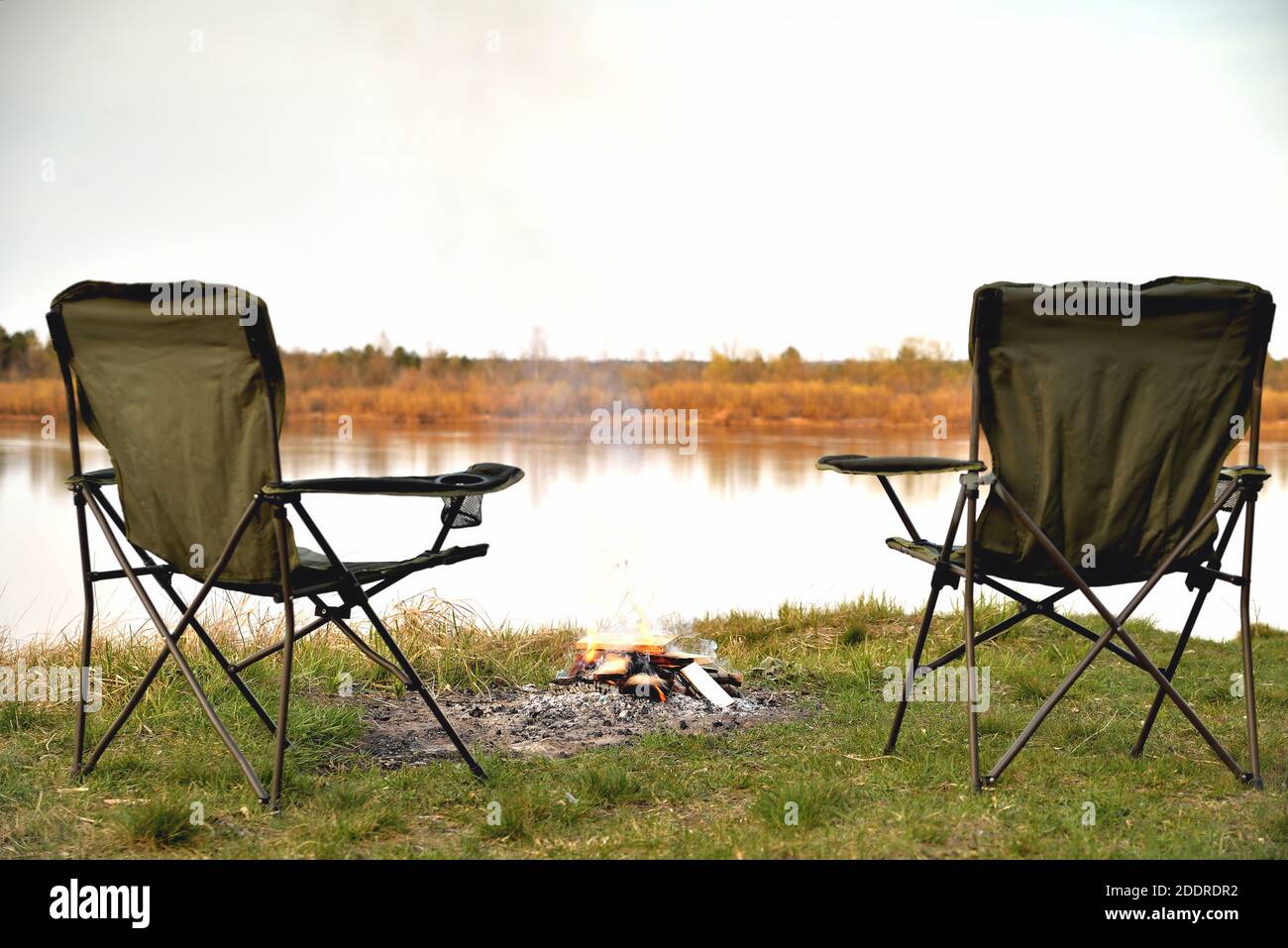 Ein Paar Touristensessel, ein Klappstuhl, ein Lagerfeuer am Flussufer am Abend bei Sonnenuntergang, Dämmerung im Herbst bei Sonnenuntergang, Entspannung und Ruhe, Stockfoto