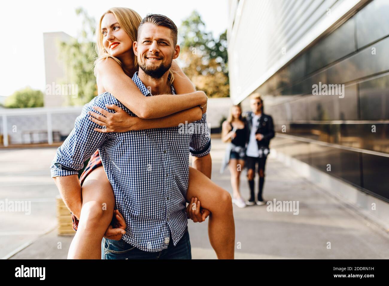 Junge Freunde haben Spaß in der Stadt, Mädchen und Jungen, Studenten gehen, im Vordergrund trägt ein Mann ein Mädchen auf dem Rücken Stockfoto