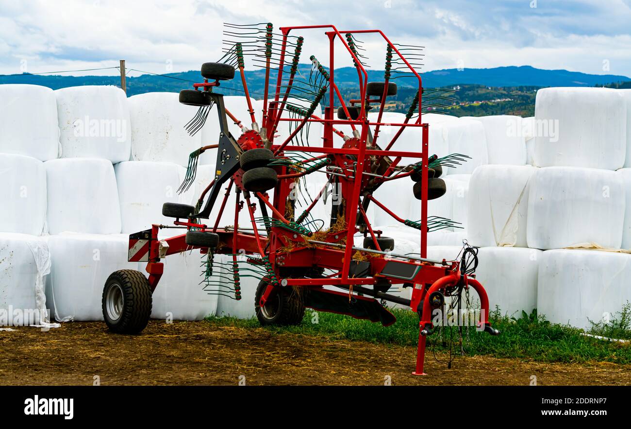 Rote Rotor Rechen Landmaschine mit Gras Heuballen Silage in weißen Kunststoff im Hintergrund eingewickelt. . Hochwertige Fotos Stockfoto