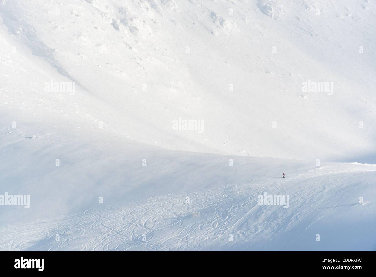 Einsamer Skifahrer, der sich in einem Skigebiet auf den Bergen ausruhen kann. Der kleine Skifahrer gibt ein Gefühl von Maßstab. Stockfoto